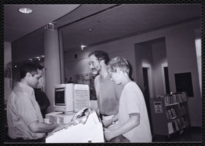 Newton Free Library, Newton, MA. Communications & Programs Office. Photograph of three people at a library service desk