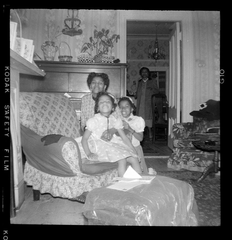 A woman posing with two girls, another woman visible in the doorway