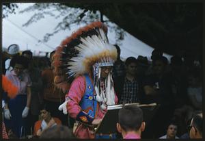 Man in feathered headdress standing at lectern among crowd of people