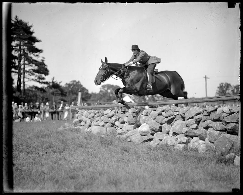 Horse and rider jumping over a low stone wall