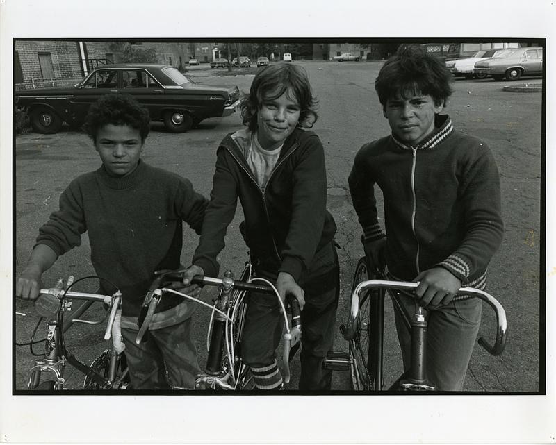 Three children posing with bicycles in a parking lot