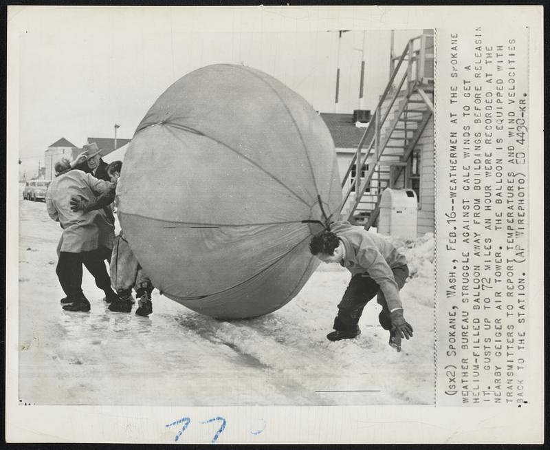 Spokane, Wash -- Weathermen at the Spokane Weather Bureau struggle against gale winds to get a helium-filled balloon away from buildings before releasing it. Gusts up to 72 miles an hour were recorded at the nearby Geiger air tower. The balloon is equipped with transmitters to report temperatures and wind velocities back to the station.