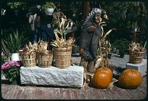 Pumpkins next to baskets of dried corn and wood sculpture of a Native American man