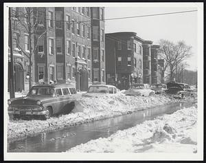 Still Blockaded against resumption of trolley bus service is Blue Hill avenue, Dorchester, shown yesterday afternoon. A narrow open stretch permits single lane traffic but the plowed under cars are directly below the wires necessary for the trolley operation.