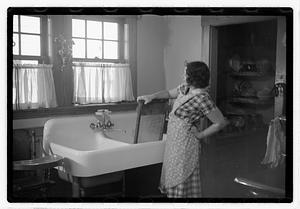 A woman standing by a sink holding a washboard