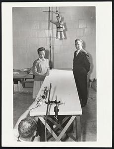 Shooting darts into "Hitler" is a device used to illustrate sound scientific principles. Here the "marksman," behind a "blow gun," explains to co-ed Betty Christman that an object "fired" directly at its target describes a curve rather than a straight line. Looking on is Dr. H. K. Schilling, lecturer-demonstrator.