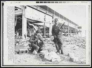 Guard Patrol Against Looters--Two Mississippi National Guardsmen patroling the Biloxi beachfront against looters, pause for a rest near a bathroom fixture ripped from the wind-damaged beachfront motel in background by Hurricane Camille. Debris from the motel is scattered on the white sand beach behind them.