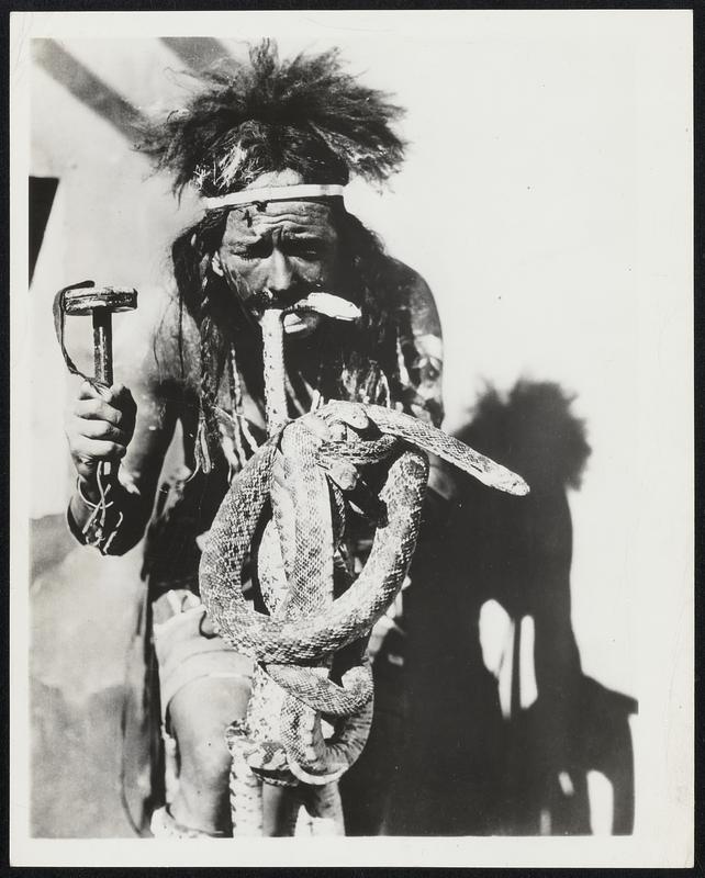 Snake Priest Regalia. August is the month the Hopi Indians hold their annual snake dances and ritual prayers for rain. In that month the Indians handle the deadly rattle-snake without apparent harm. During the rest of the year the Hopis avoid the snakes as much as any one else. This picture made some years back shows the authentic regalia of a snake priest ready for the rain dance. The painted wearer is not an Indian but a Prescott, Arizona, businessman who belongs to the "Smokis" a group pledged to keep alive the culture and customs of the American Indians.