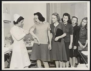 Students at U. of C. Test Flu Vaccine. The new type of Influenza vaccine, discovered by two Rockefeller Foundation research workers, Dr. Edwin H. Lennette and F.L. Horsfoll, is being administered to 500 students at the University of Chicago, as a possible preventive of Influenza. Because of recent widespread outbreaks of the flu a good opportunity to test the vaccine under actual conditions can be made. The 500 students inoculated will be watched closely. Their resistance to the disease will be checked against the student body  as a whole in the event any large number cases of flu occur among the students. Photo shows Coeds lineup as Martha Cooley, R.N. gives an injection to Jean Roff, freshman student at the University of Chicago.