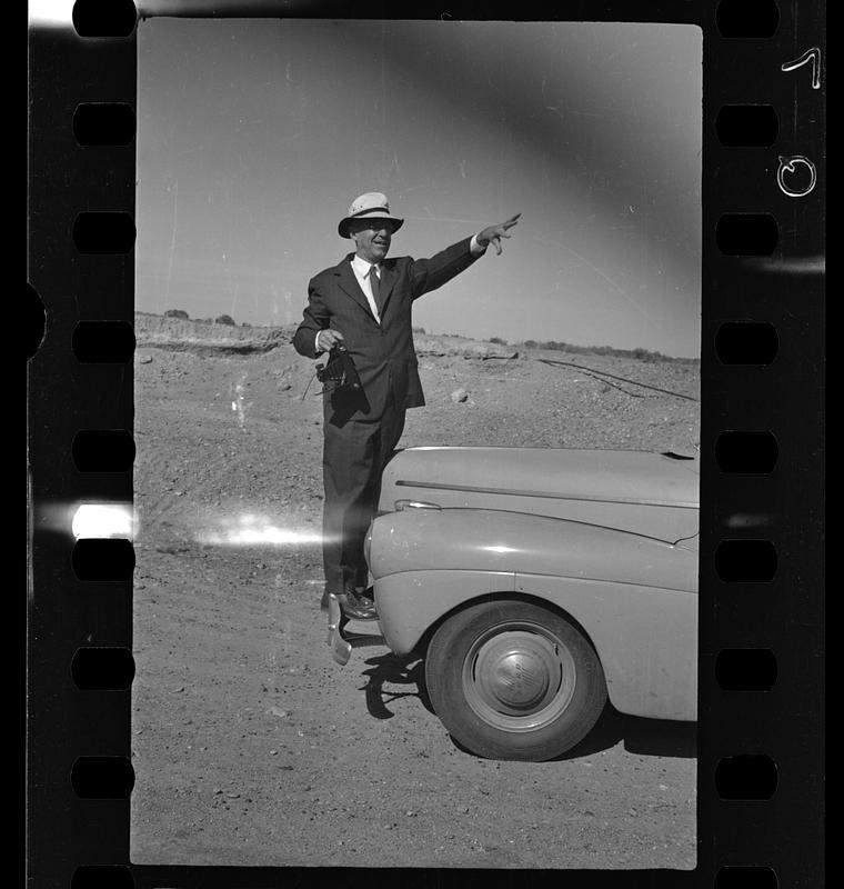 Man holding camera next to car in the desert, likely New Mexico