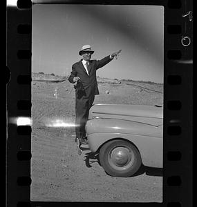 Man holding camera next to car in the desert, likely New Mexico