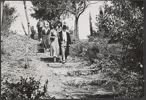 Serge Koussevitzky walking with an unidentified woman down stairs, a group of people behind them