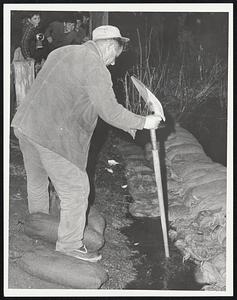 Morey Dam - Taunton - Taunton City employee Steve Punda measures water with shovel handle, water rising past sandbags ready to fill with clay.