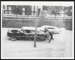 Game Girls trudge through the deep snow on Dartmouth St. in front of steps of the Boston Public Library in Copley Square today (left photo). At right, trio of men attempt to push car stuck in the Huntington Ave. underpass at Massachusetts Ave. This was common sight in the Hub.