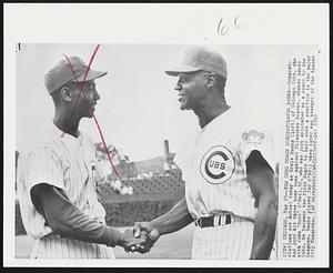 Chicago – New Cubs Coach Congratulates Banks – Congratulations are mutual today as Ernie Banks (left) to Chicago Cubs, who had just hit three home run against Milwaukee Braves, shakes hands with John “Buck” O’Neil, 50, who was just appointed as a coach by the Cubs. He becomes the first Negro to hold such a position in the major leagues. Banks played for O’Neil when later was manager of the Kansas City Monarchs.