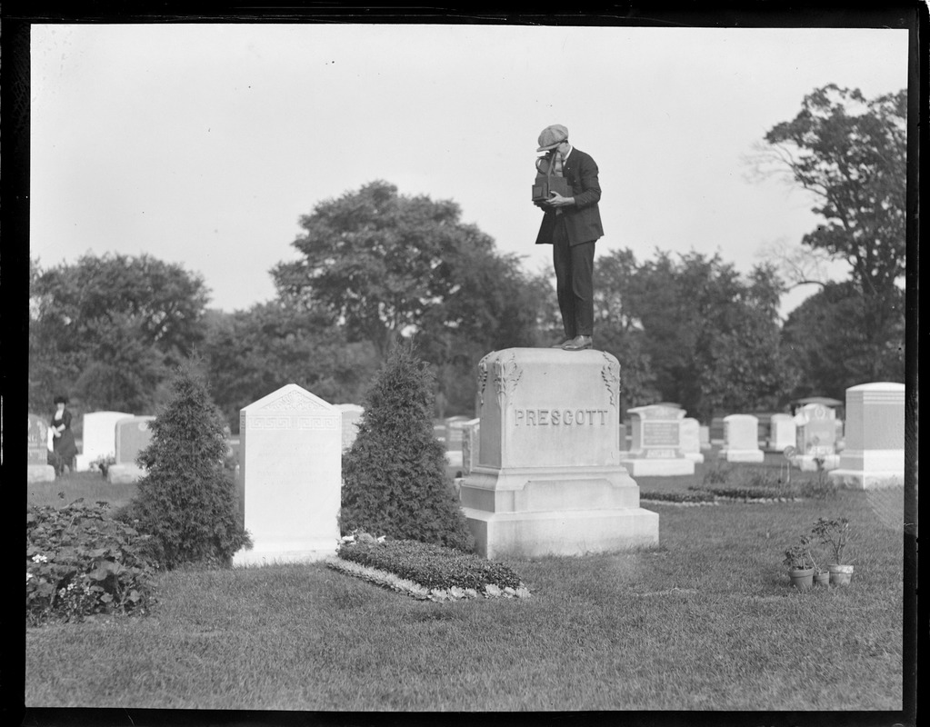 Herbert Stier of the Boston Post stands on tomb stone to make a funeral picture