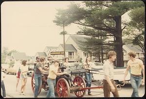 Men and women hauling antique fire apparatus in parade