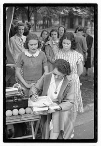 Two young women looking down at a woman signing a piece of paper