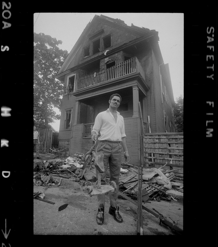 Luis Carvalno holding burned tricycle outside of ruins of house fire on Gayland Street, Roxbury, in which seven of his relatives died