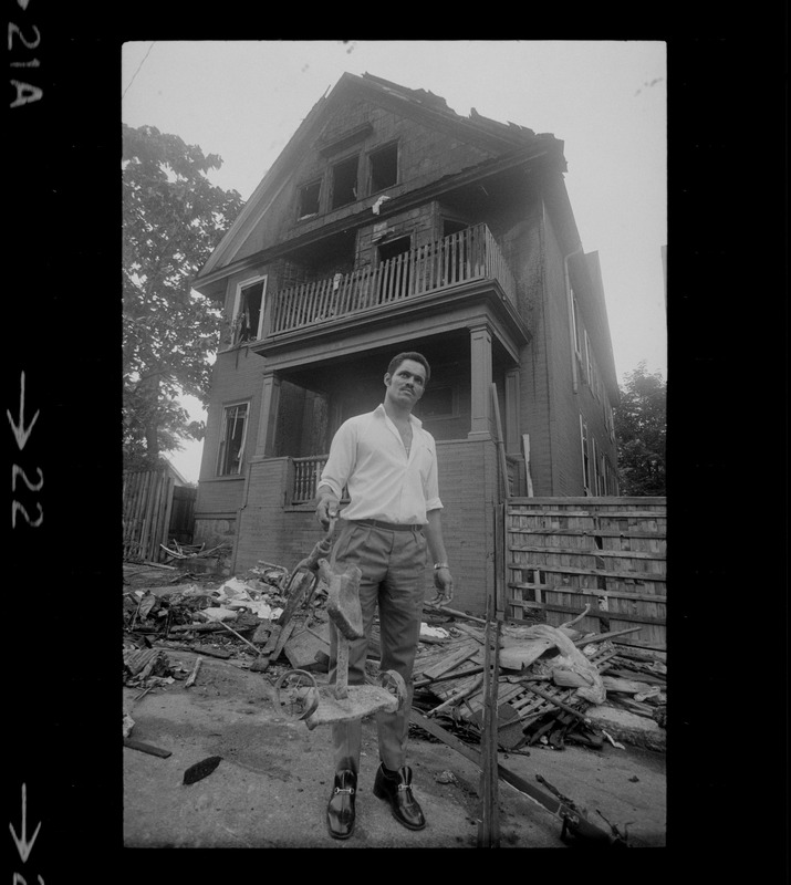 Luis Carvalno holding burned tricycle outside of ruins of house fire on Gayland Street, Roxbury, in which seven of his relatives died