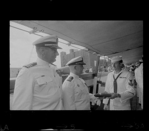 Commander Jack L. Reifschneider receiving flag from sailor as Commander Hugh Moore watches on USS Constitution