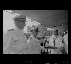 Commander Jack L. Reifschneider receiving flag from sailor as Commander Hugh Moore watches on USS Constitution