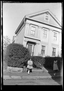 A girl poses in front of a house and shrubs