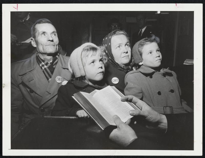 Deep In Thought – Kusma Kandaurow, 61, and his wife, Sofie, 41, and their children, Hanna, 9, and Sonja, 5, listen intently as a clergyman reads Scripture following their arrival in New York City. They arrived with other refugees aboard the Navy Transport General Langfitt.