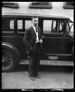 Unidentified man standing by a car, cigarette in hand