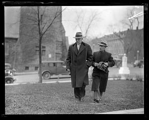 Two men, one holding a camera, walking outside