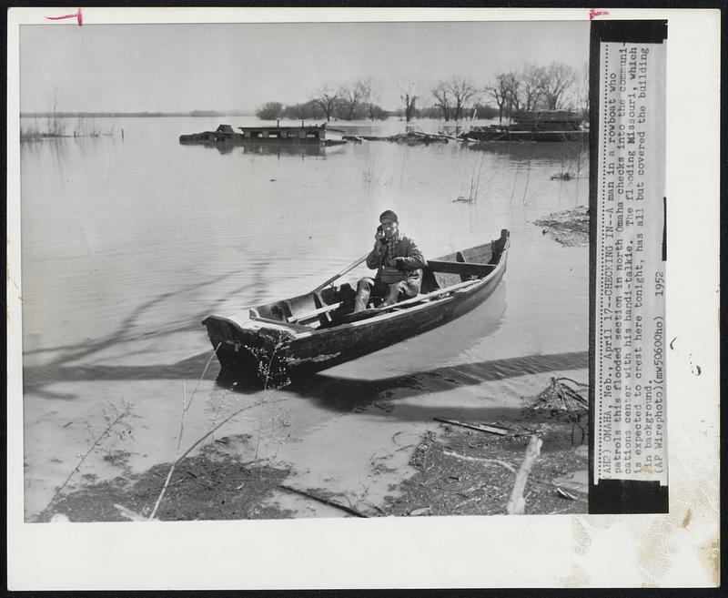 Checking In--A man in a rowboat who patrols his flooded section in north Omaha checks into the communications center with his handi-talkie. The flooding Missouri, which is expected to crest here tonight, has all but covered the building in background.