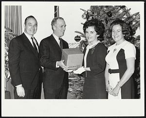 Mayor Kevin H. White hands over one of the 659 Christmas packages for Boston servicemen in Vietnam to Carole Dugroo of United Airlines, United is flying the packages free of charge to San Francisco on the first leg of their journey. Also shown are Frank J. Hadley (L) of Wilson & Co., which provided the bulk of the package at cost, and Theresa Carroll of Harbor National Bank of Boston, which acted as treasurer for the privately funded program.