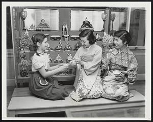 Observe Japanese Doll Festival. Dolls which can be played with only once a year, on March 3, are the background for tea at the Children's Museum, Boston, as Yasuko Ohashi, (center), of Yokohama and Kuniko Shiobara (right), of Tokyo, students at Newton College of the Sacred Heart, observe traditional ceremonies of the annual Japanese Doll Festival with young Museum visitor, Kathleen Maloney, 10, of Jamaican Plain, as their guest.