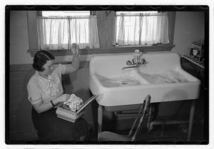 A woman sewing next to a sink full of laundry