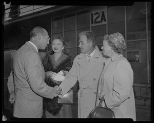 Milburn Stone shaking hands with man at airport as Amanda Blake and Miss Elizabeth Storer look on