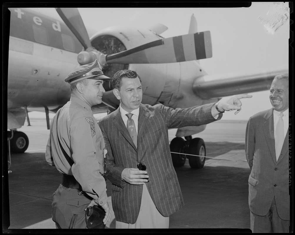 Jack Webb pointing and talking to a state police officer in front of airplane as city greeter Jack Brown looks on