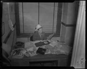 Gene Autry seated at desk with photos, drawings, albums, and packages, most likely fanmail