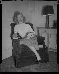 Barbara Ann Scott seated with glass and newspaper in hotel room at Copley Plaza