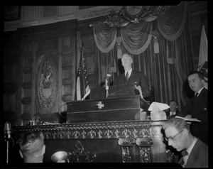 Gov. Christian Herter speaking from podium of House Chamber at State House, with Lt. Gov. Sumner G. Whittier seated behind