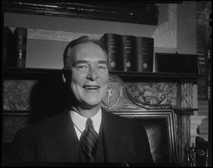 Gov. Christian Herter seated in front of fireplace