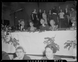 Gov. Christian Herter, Mary Pratt Herter, and others seated at banquet table with performers behind them