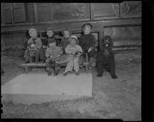 Group of small children seated on bench with dog and holding models of a duck and goose
