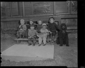 Group of small children seated on bench with dog and holding models of a duck and goose