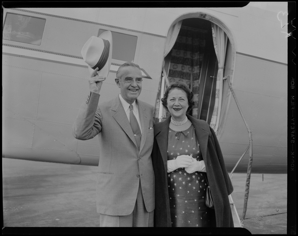 Averell Harriman raising his hat, with wife Marie Norton Harriman next to him and plane in background