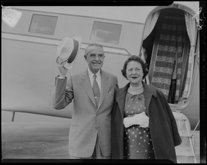 Averell Harriman raising his hat, with wife Marie Norton Harriman next to him and plane in background