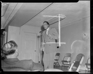 Billy Graham speaking at microphone with folding chairs behind him