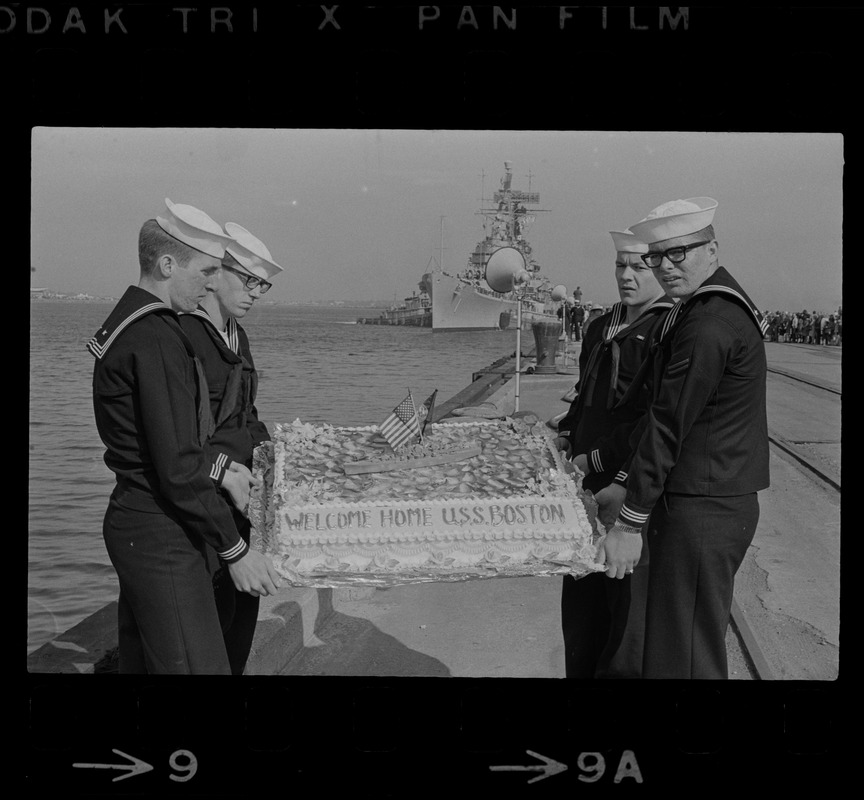 Sailors hold cake as the guided missile heavy cruiser U. S. S. Boston comes alongside pier at South Boston Naval Annex