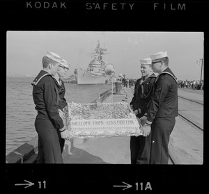Sailors hold cake as the guided missile heavy cruiser U. S. S. Boston comes alongside pier at South Boston Naval Annex