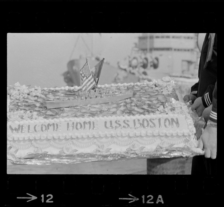 Sailors hold cake as the guided missile heavy cruiser U. S. S. Boston comes alongside pier at South Boston Naval Annex