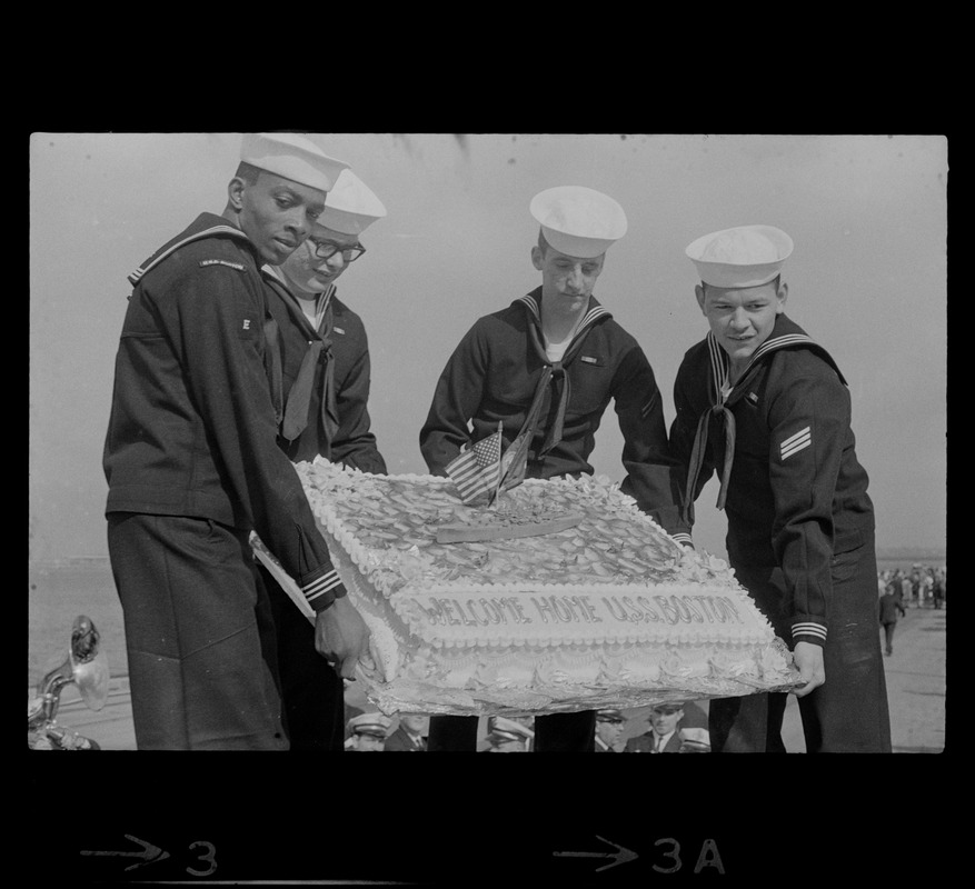 Sailors hold cake as the guided missile heavy cruiser U. S. S. Boston comes alongside pier at South Boston Naval Annex